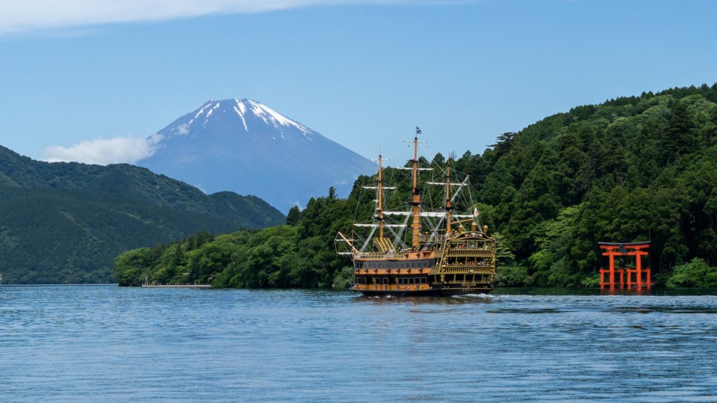 Scenic view of Lake Ashi in Hakone, Japan, featuring a pirate-style cruise ship, the iconic red torii gate of Hakone Shrine, and Mount Fuji in the background.