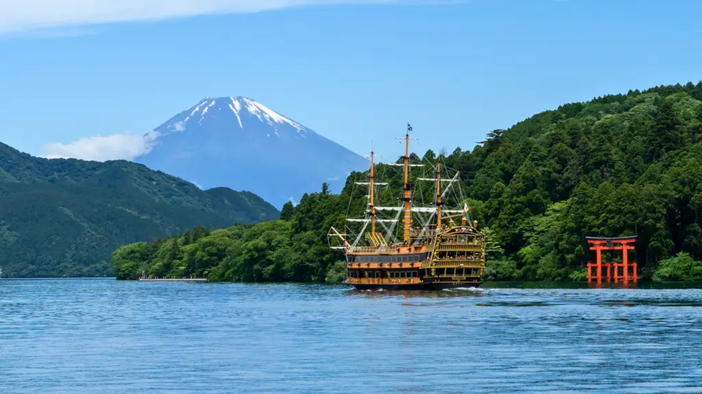 Lake Ashi in Hakone, Japan, featuring a pirate-style sightseeing cruise ship, the iconic red torii gate of Hakone Shrine, and Mount Fuji in the background.