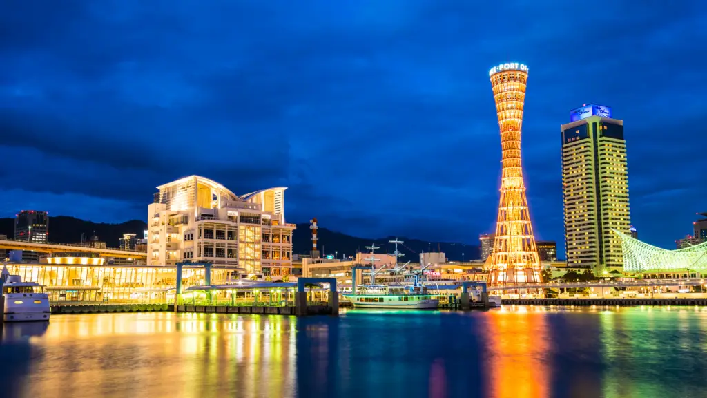 Kobe Port Tower illuminated at night, reflecting on the waterfront in Kobe, Japan. The city skyline, boats, and modern architecture create a vibrant and picturesque scene.