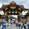 Tourists walking through the ornately decorated Karamon Gate at Nijo Castle in Kyoto, Japan. The historic wooden gate features intricate carvings and gold embellishments, reflecting the grandeur of the Edo period.