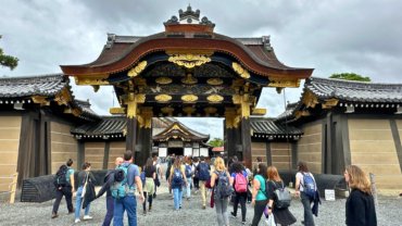 Tourists walking through the ornately decorated Karamon Gate at Nijo Castle in Kyoto, Japan. The historic wooden gate features intricate carvings and gold embellishments, reflecting the grandeur of the Edo period.