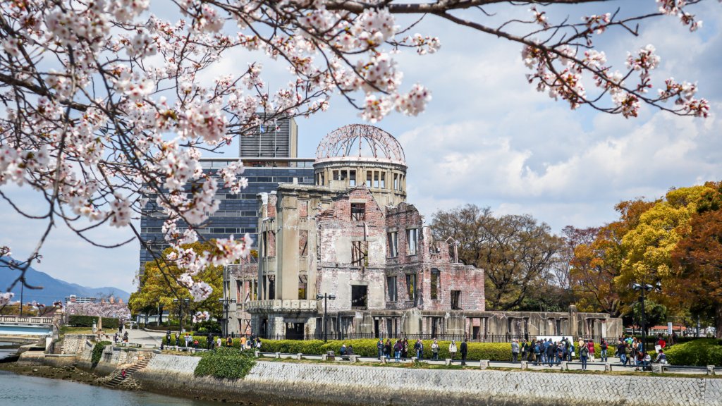 The Hiroshima Peace Memorial (Atomic Bomb Dome) framed by cherry blossoms, standing as a symbol of remembrance and resilience along the Motoyasu River in Hiroshima, Japan.