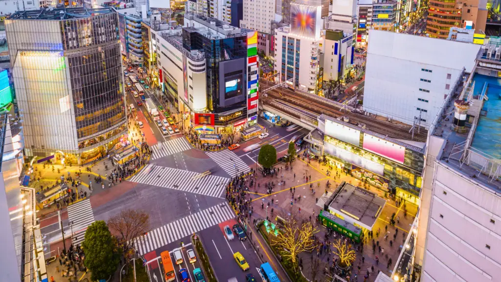 Aerial view of Shibuya Crossing in Tokyo, Japan, at dusk, showcasing the bustling intersection, neon lights, and urban energy of one of the world’s busiest pedestrian crossings.