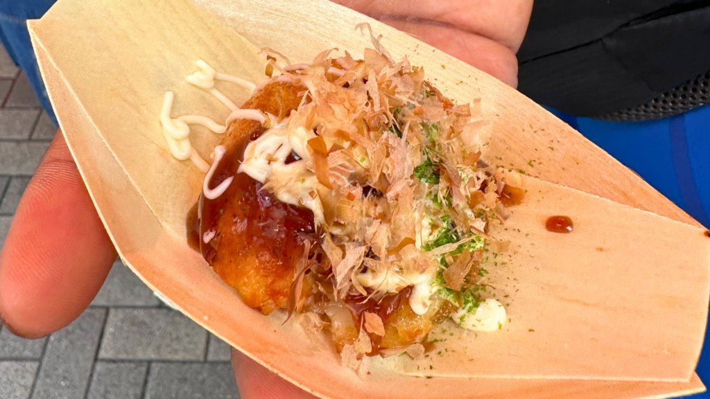 A delicious serving of takoyaki, Osaka’s famous octopus-filled street food, topped with savory sauce, mayonnaise, bonito flakes, and seaweed, served in a traditional paper tray.