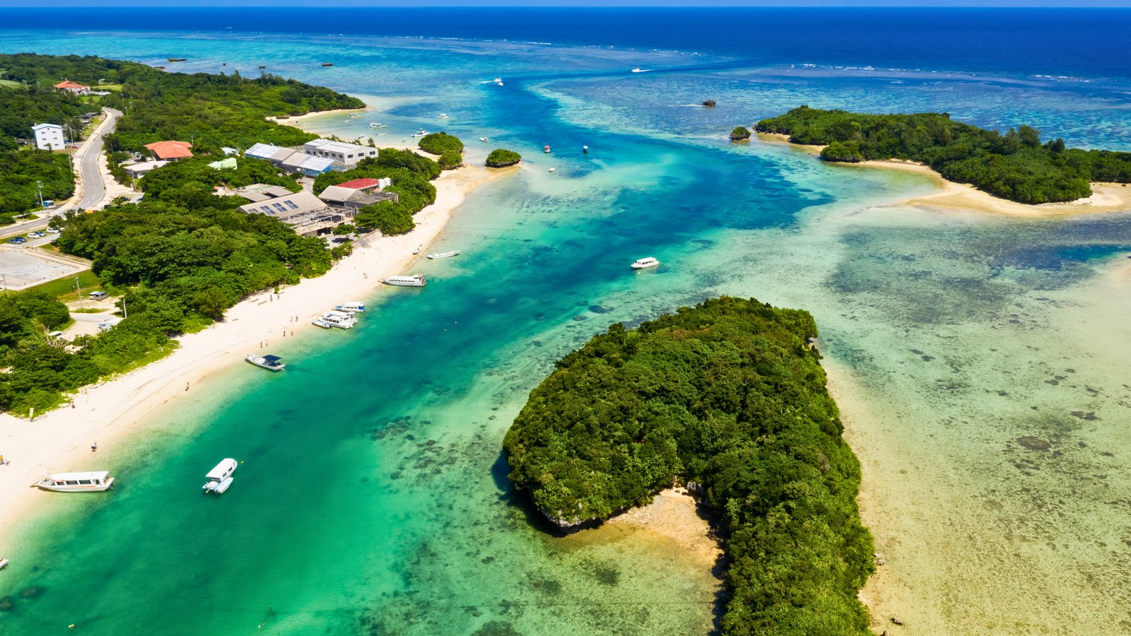 Aerial view of Kabira Bay in Ishigaki Island, Japan, showcasing crystal-clear turquoise waters, lush green islands, and white sandy beaches with boats floating nearby.