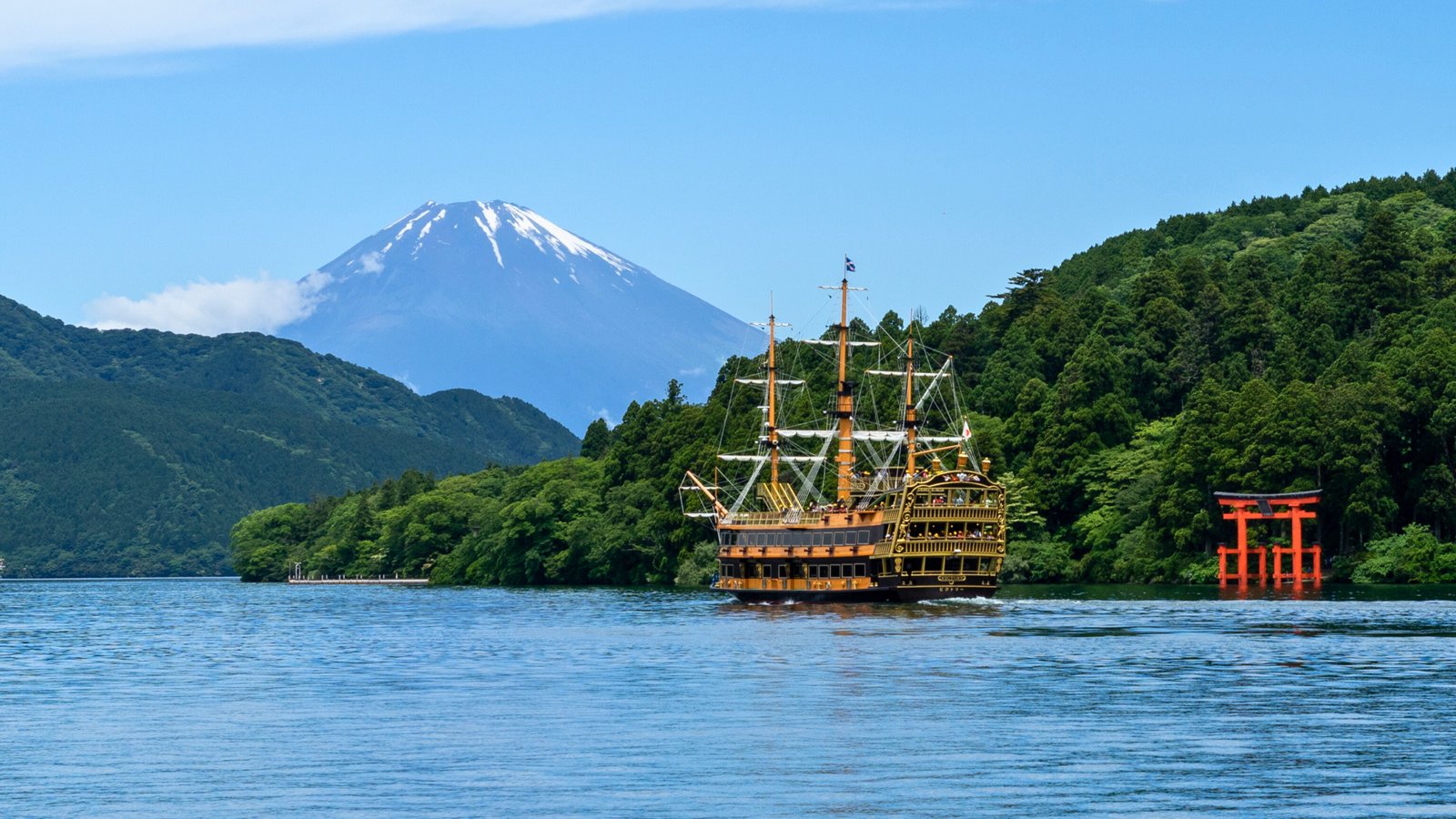 Lake Ashi in Hakone A scenic view of Lake Ashi in Hakone, featuring a pirate sightseeing cruise ship, the iconic red torii gate of Hakone Shrine, and Mount Fuji in the background.